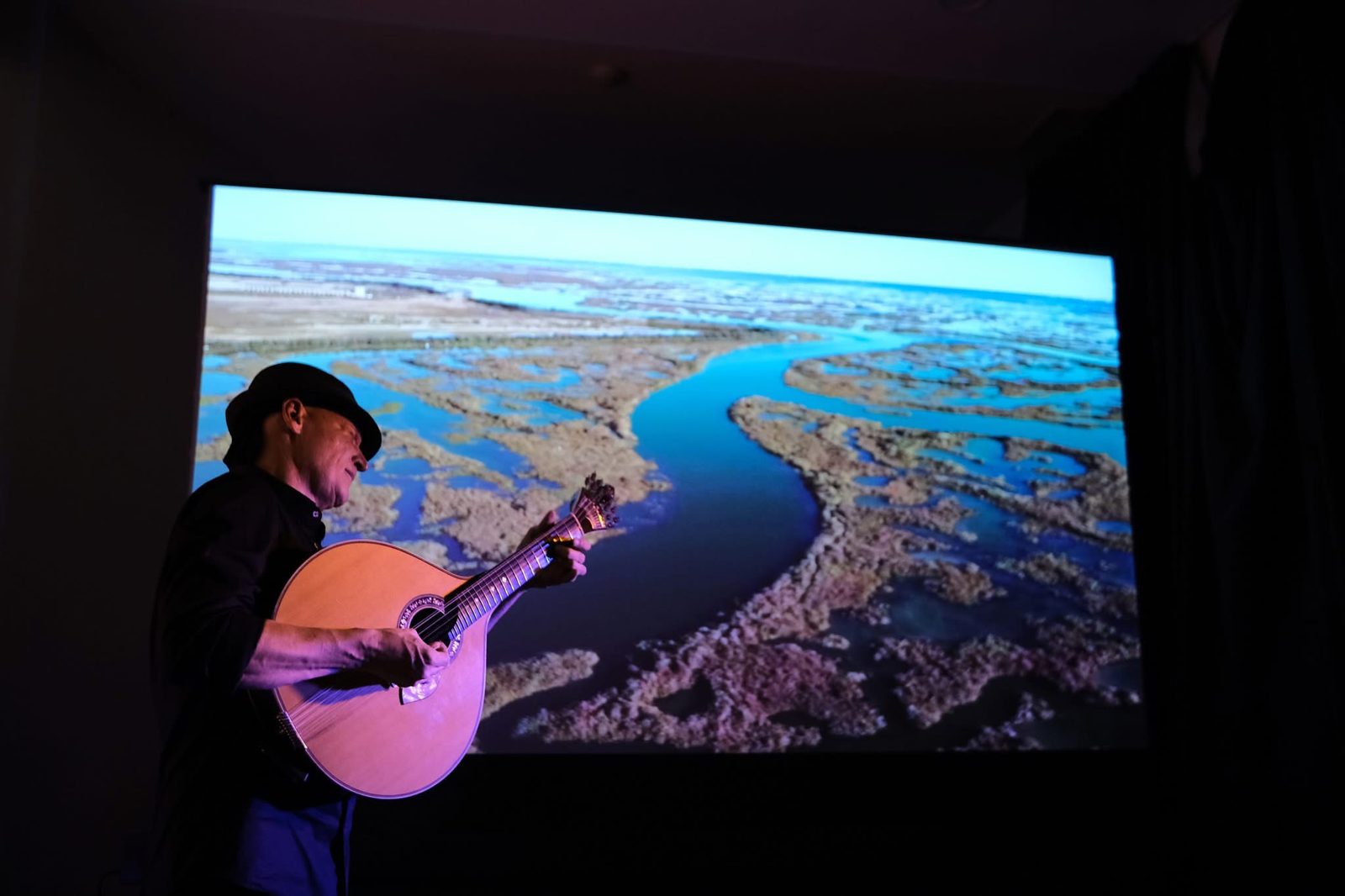 João Cuña plays the Portuguese guitar with the Ria Formosa projected behind him